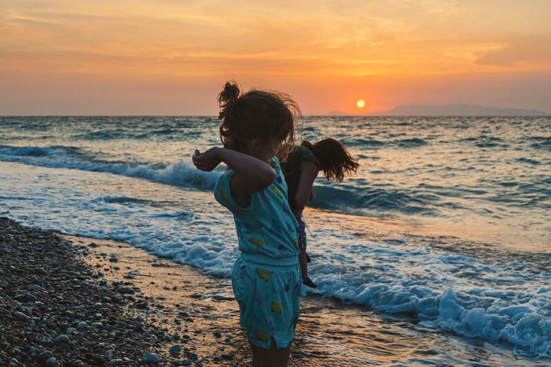 Girl standing on beach against sky during sunset