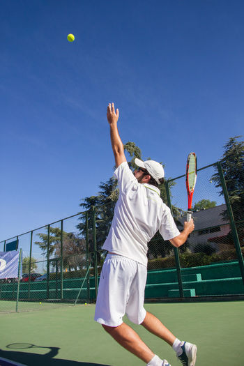 Man playing tennis on court against blue sky
