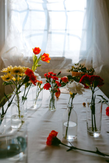 Glasses of fresh tulips and carnations in water placed on table for making bouquets