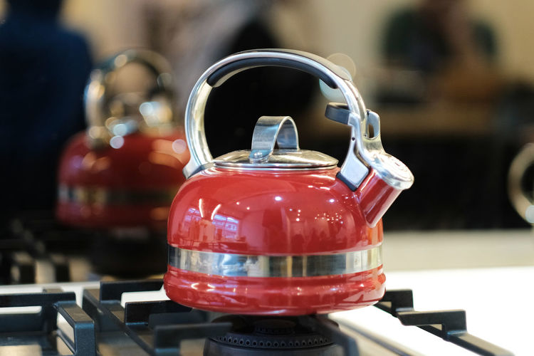 A still life view of a red kettle on a stove in a kitchen