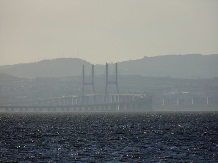 Bridge over sea by mountains against clear sky