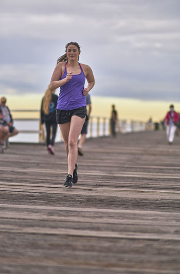 Young woman running on pier against sky during sunrise