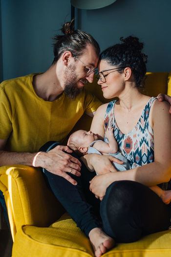 Woman sitting on yellow sofa at home holding her new born baby