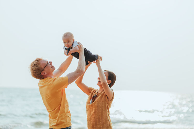 Cheerful family standing on beach against sky