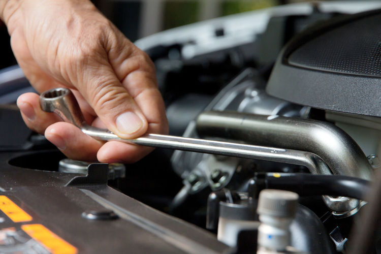 Cropped hand of mechanic repairing car engine with wrench