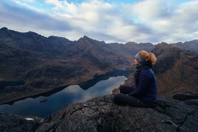 Woman sitting on rock looking at mountains against sky