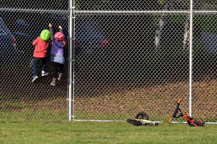 Rear view of siblings climbing on chainlink fence