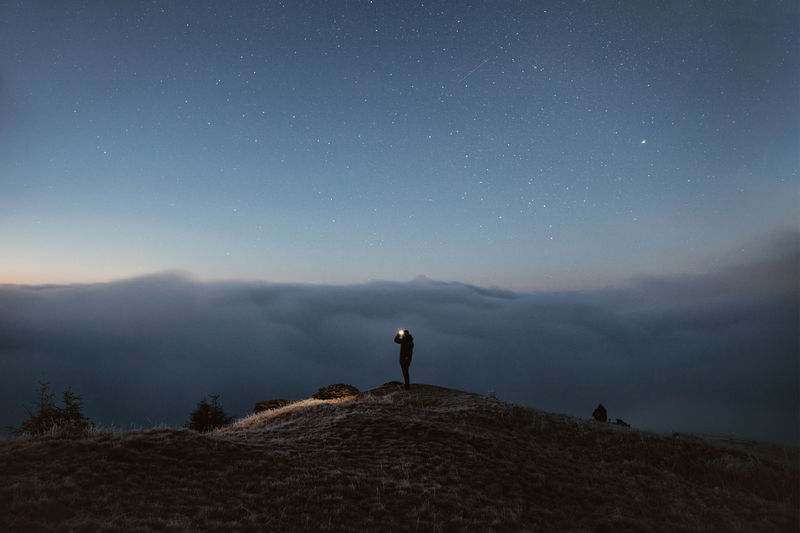 Person standing on the mountain above the clouds during the night