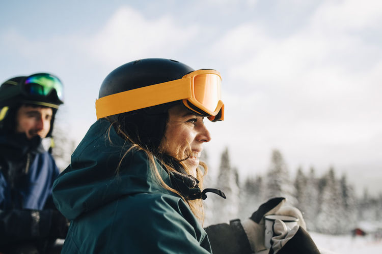Smiling woman wearing ski goggles while holding coffee cup during winter