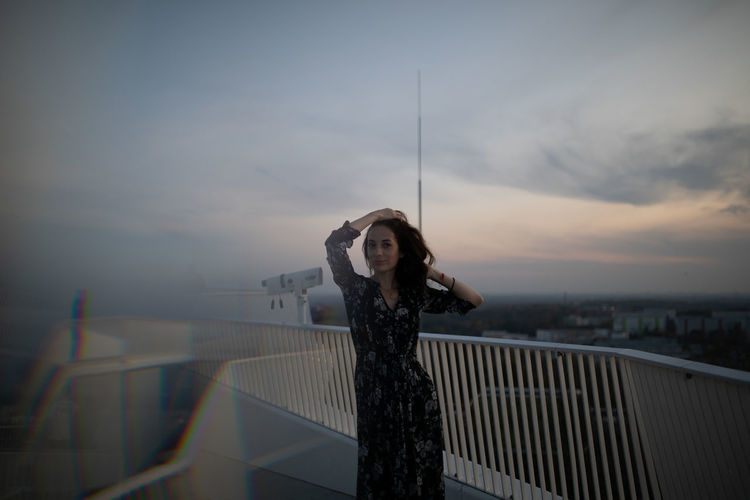 Portrait of woman standing by railing against sky during sunset