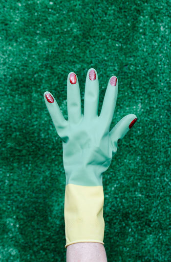 Hand with plastic glove and nails painted red on a green background