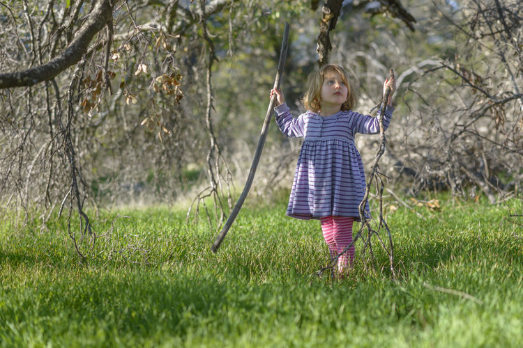 Girl holding sticks while standing on grassy field
