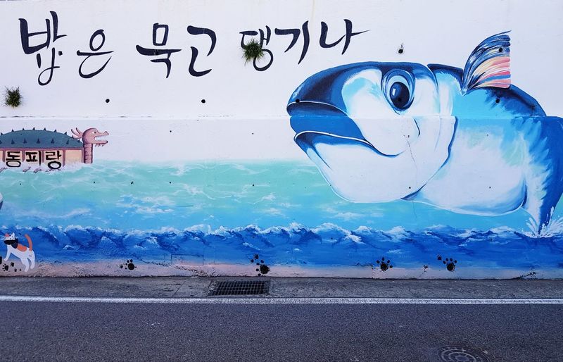 Graffiti on wall by sea against blue sky