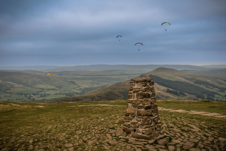 Paragliders over landscape against cloudy sky at derbyshire