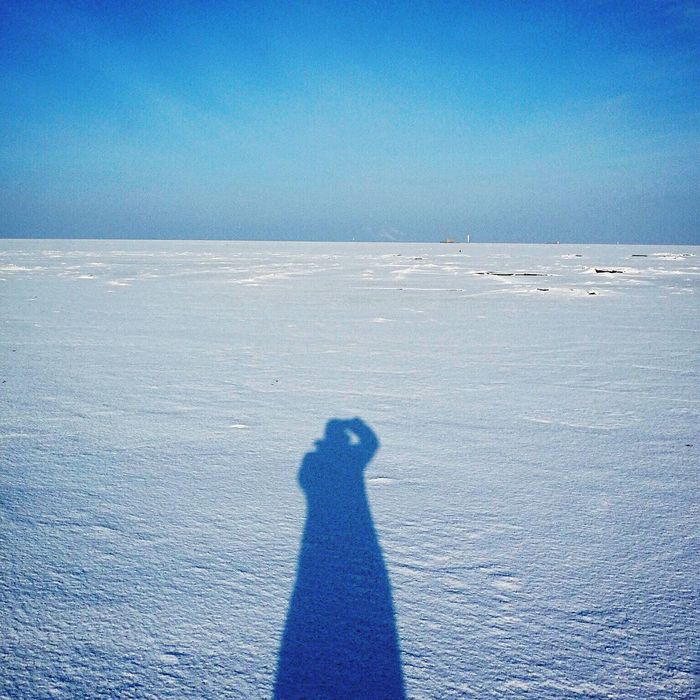 Shadow of man on snow covered field against clear blue sky