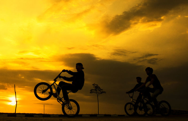 Silhouette people riding bicycle against sky during sunset