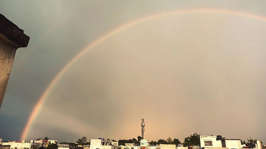 Low angle view of rainbow over buildings in city against sky