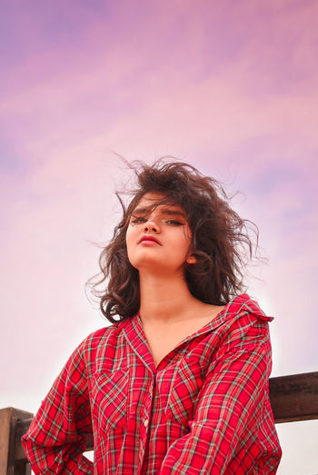 Portrait of beautiful woman with tousled hair standing against sky