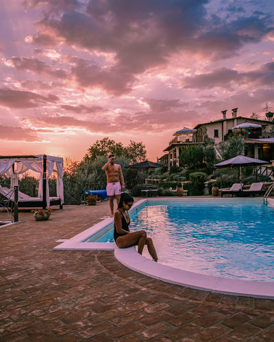 Woman sitting in swimming pool against sky during sunset