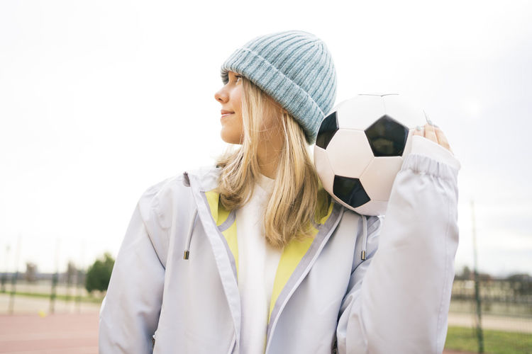 Teenage girl wearing knit hat standing with soccer ball