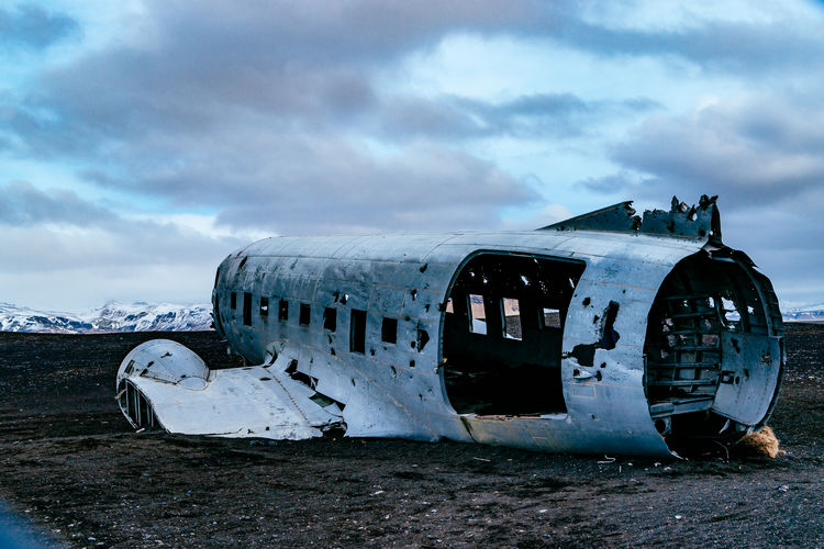 Abandoned military airplane at beach against cloudy sky during winter