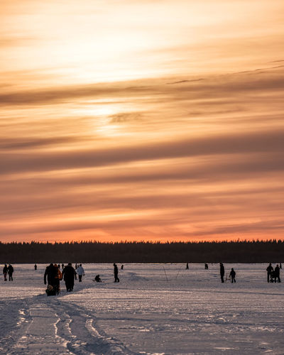 People walking on snow covered landscape during sunset