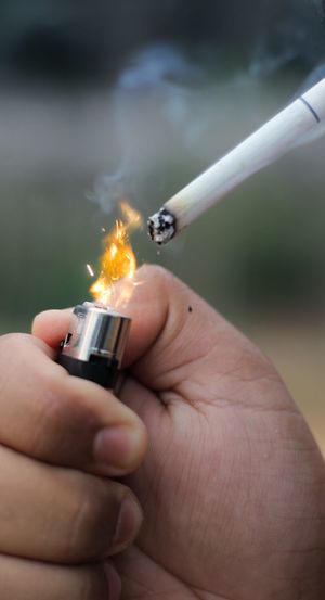 Close-up of hand holding cigarette against blurred background