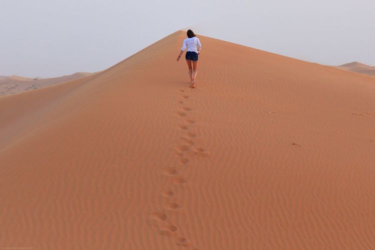 Rear view of woman walking on sand dune at desert