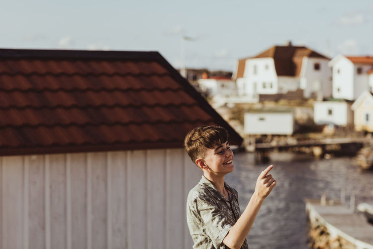 Smiling teenage boy pointing while standing against cabin
