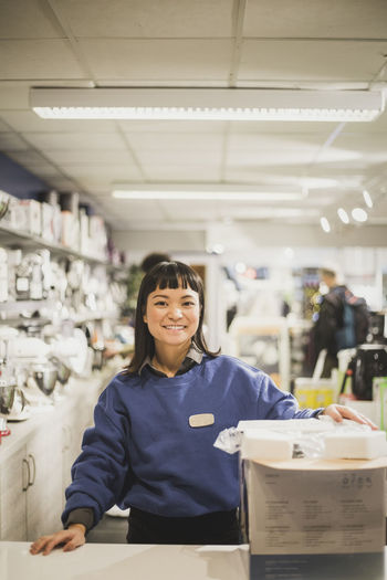 Portrait of smiling saleswoman with appliance standing in electronics store