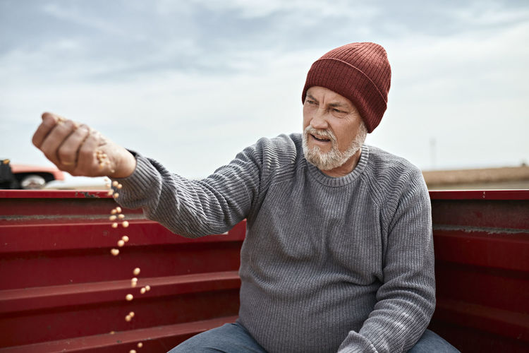 Farmer wearing knit hat examining cultivated soybean against clear sky