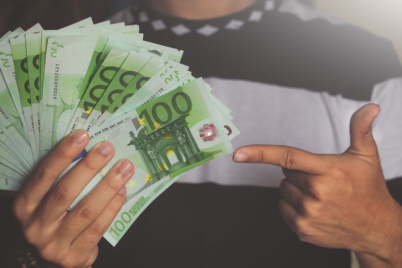 Midsection of man pointing at fanned out green paper currencies