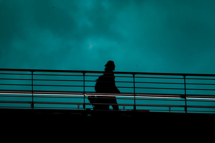 Low angle view of silhouette man walking by railing against sky