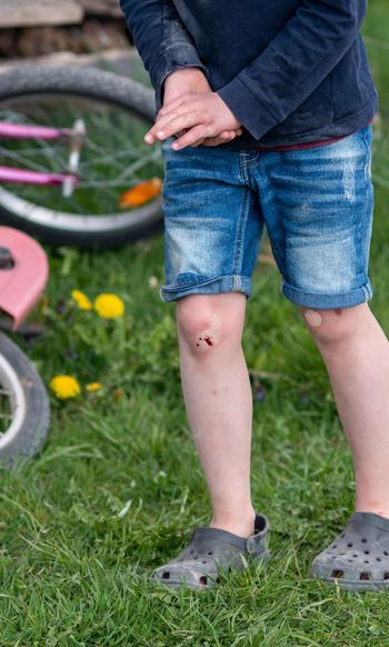 Low section of boy with scraped knee standing on grass