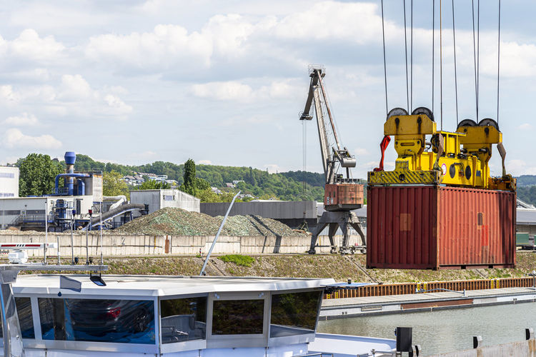 A container gantry crane on a rail loads the container into a barge standing on the banks of river. 