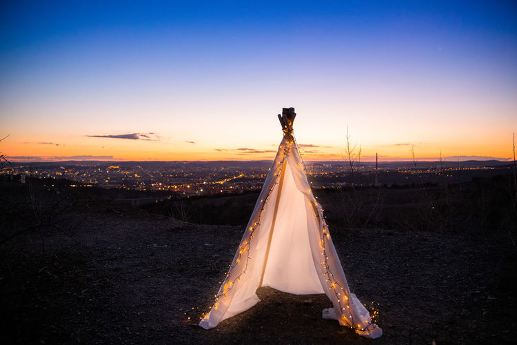 Illuminated tent on field against sky at sunset