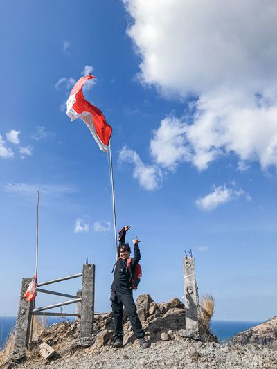 Man standing by flag on rock against sky