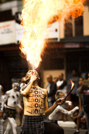 Shirtless young man blowing fire while standing on city street