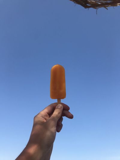 Cropped hand of person holding popsicle against clear sky