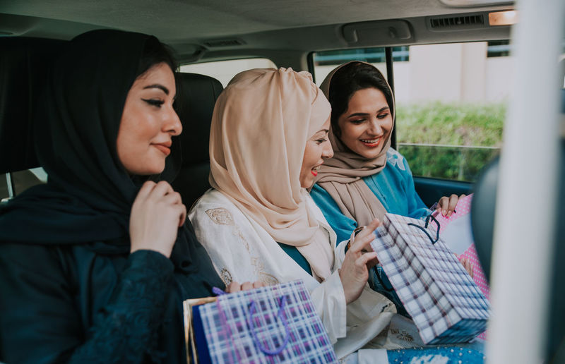 Cheerful women wearing hijab sitting in car with shopping bags