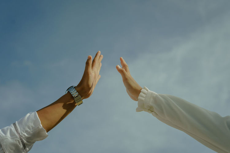 Low angle view of couple holding hands against sky