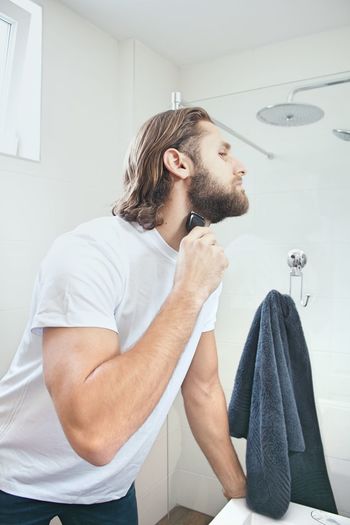 Young man shaving beard at domestic bathroom