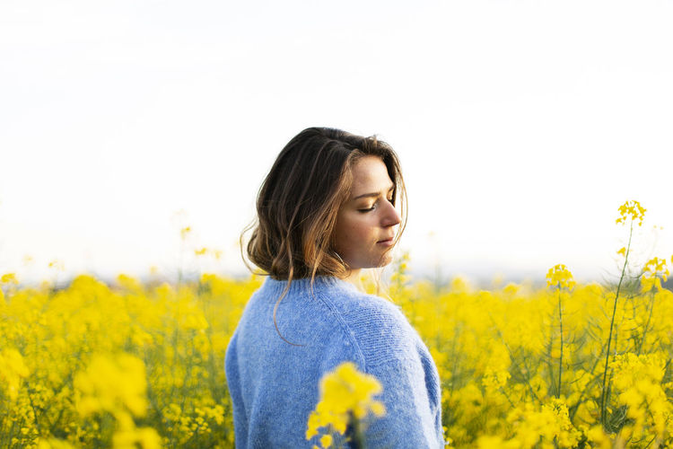 Beautiful woman standing on yellow flowers field against sky