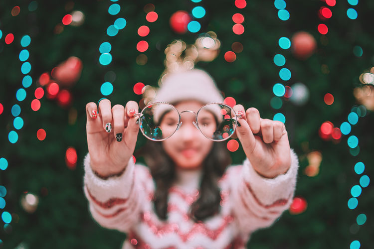 Woman holding eyeglasses while standing by christmas tree