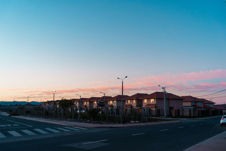 Street by buildings against sky at sunset