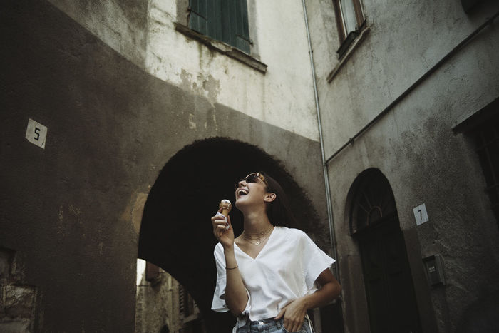 Young woman with ice cream standing against built structure