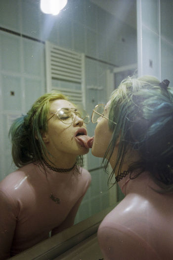 Young woman with freckles and pierced licking mirror in bathroom