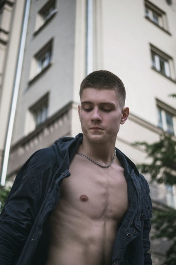 Low angle view of young man with fully unbuttoned shirt against building