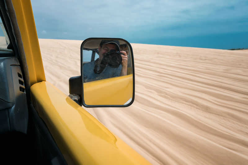 Man photographing while reflecting on side-view mirror of car