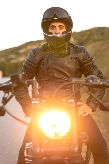 Biker in helmet sitting and relaxing on vintage motorcycle on sunset.